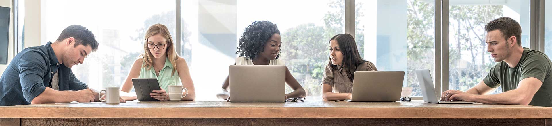 Two man nd three woman sitting down looking at laptop screen and tablet screen