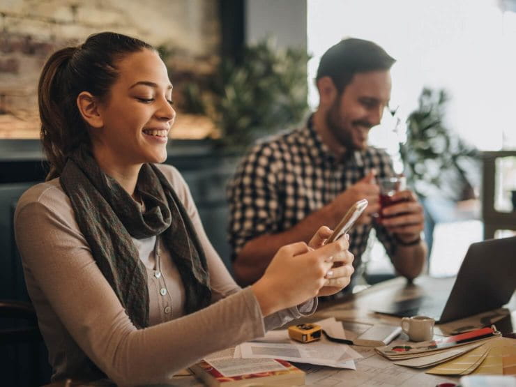 Smiling woman and man working on mobile phone and laptop